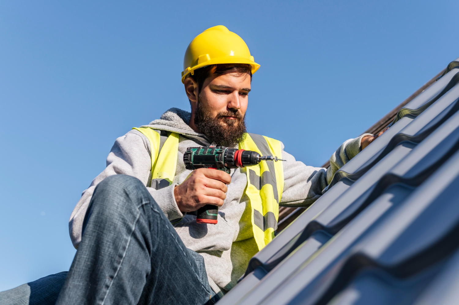 Summit Roofing technician fastening a standing seam metal roof under a clear Colorado sky