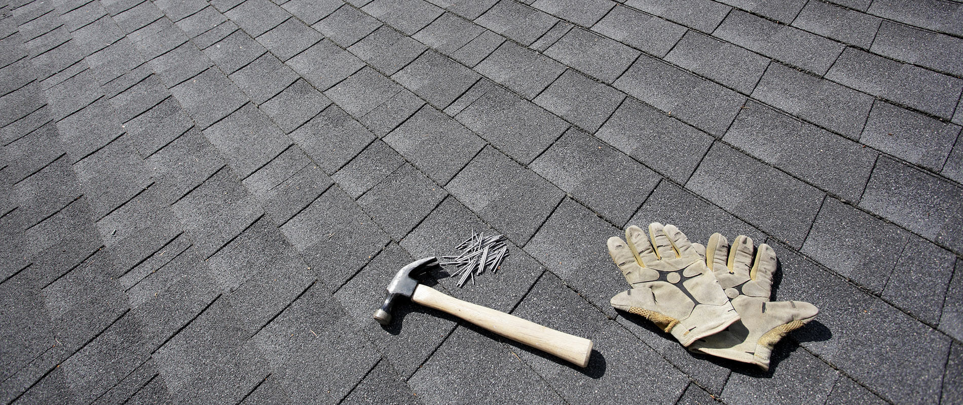 Architectural asphalt shingle roof with a hammer, roofing nails and work gloves laid out mid project